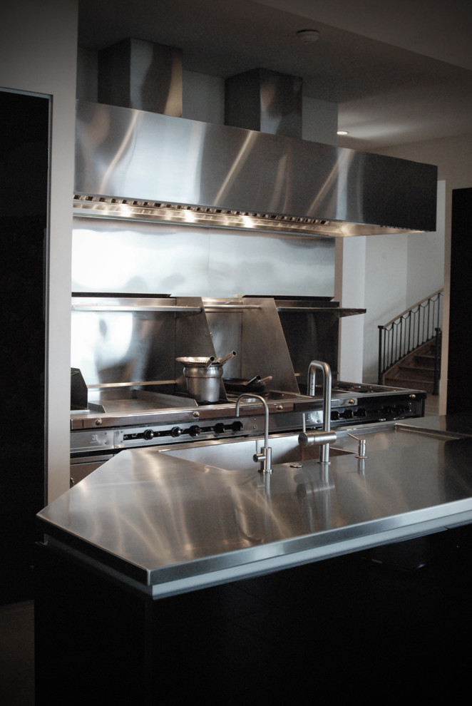 Photo of a mid-sized industrial u-shaped eat-in kitchen in Other with an integrated sink, flat-panel cabinets, black cabinets, stainless steel benchtops, metallic splashback and with island.