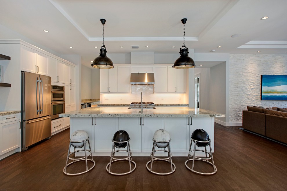 Large transitional l-shaped eat-in kitchen in Miami with shaker cabinets, white cabinets, white splashback, stainless steel appliances, an undermount sink, recycled glass benchtops, subway tile splashback, dark hardwood floors and with island.