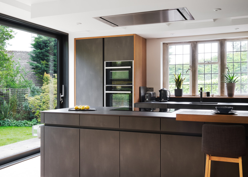 Design ideas for a large contemporary galley eat-in kitchen in Gloucestershire with a single-bowl sink, flat-panel cabinets, grey cabinets, solid surface benchtops, grey splashback, black appliances, porcelain floors, with island, beige floor and grey benchtop.