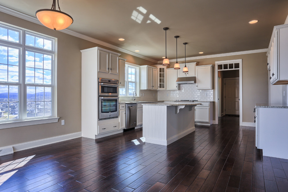 Inspiration for a mid-sized traditional l-shaped eat-in kitchen in Chicago with recessed-panel cabinets, white cabinets, granite benchtops, white splashback, ceramic splashback, stainless steel appliances, dark hardwood floors and with island.