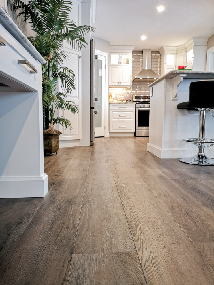 Mid-sized transitional u-shaped light wood floor and brown floor enclosed kitchen photo in Toronto with an undermount sink, raised-panel cabinets, white cabinets, granite countertops, beige backsplash, glass tile backsplash, stainless steel appliances, a peninsula and gray countertops