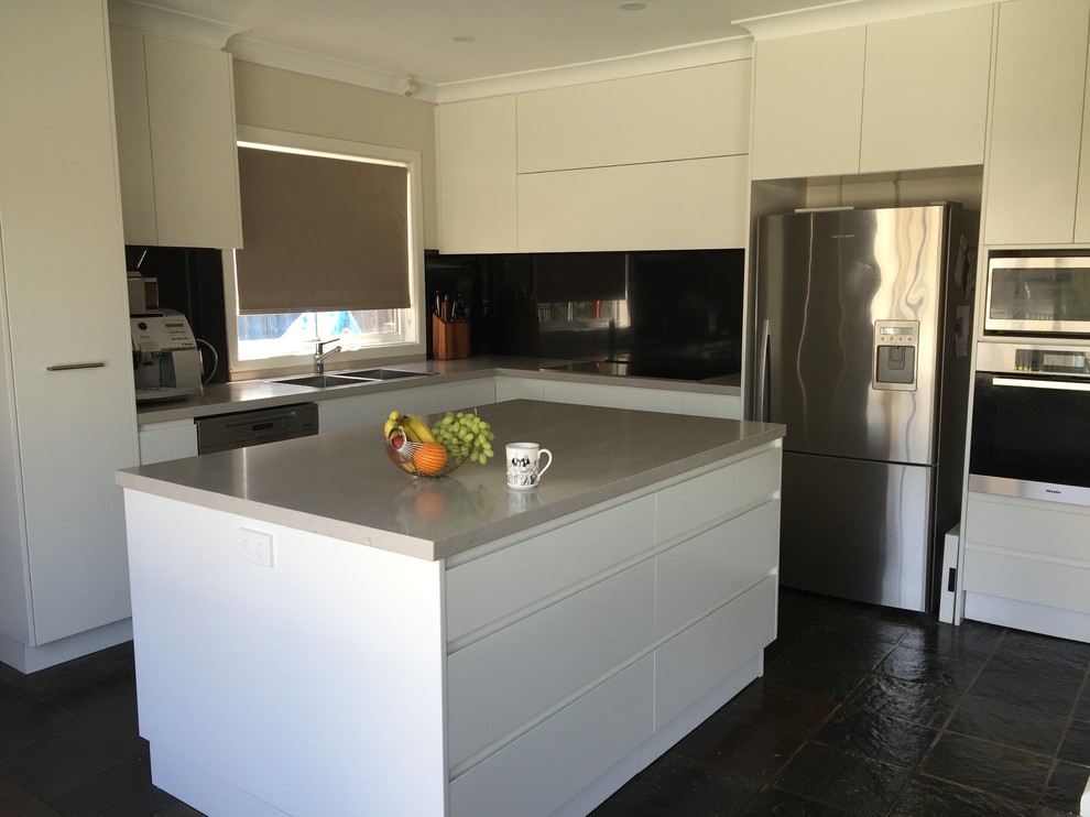 Design ideas for a large contemporary l-shaped eat-in kitchen in Sydney with an undermount sink, flat-panel cabinets, white cabinets, quartz benchtops, black splashback, glass sheet splashback, stainless steel appliances, slate floors and with island.