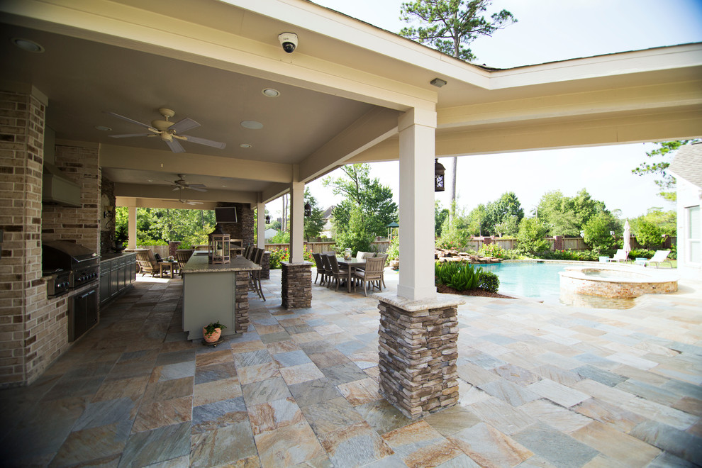 This is an example of a large traditional backyard patio in Houston with an outdoor kitchen, natural stone pavers and a roof extension.