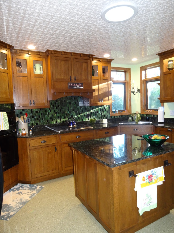 Photo of a mid-sized arts and crafts u-shaped separate kitchen in Omaha with an undermount sink, flat-panel cabinets, dark wood cabinets, granite benchtops, green splashback, glass tile splashback, black appliances, linoleum floors and with island.