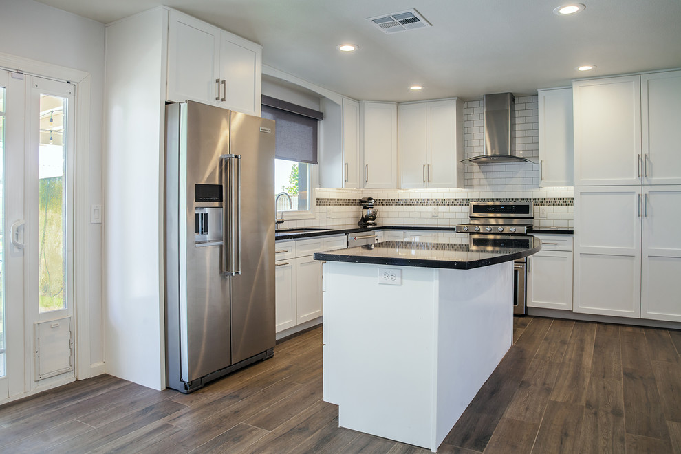 Large transitional l-shaped porcelain tile and brown floor eat-in kitchen photo in Phoenix with an undermount sink, recessed-panel cabinets, white cabinets, quartz countertops, black backsplash, ceramic backsplash, stainless steel appliances and an island
