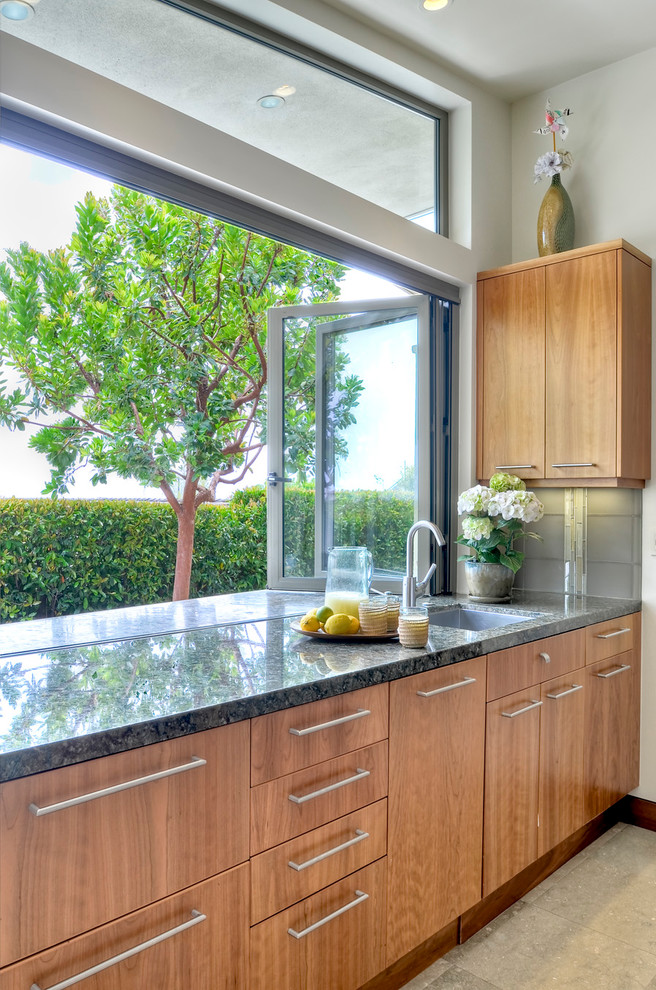 Photo of a large contemporary kitchen in San Diego with a single-bowl sink, flat-panel cabinets, medium wood cabinets, granite benchtops, grey splashback, glass tile splashback, panelled appliances and limestone floors.
