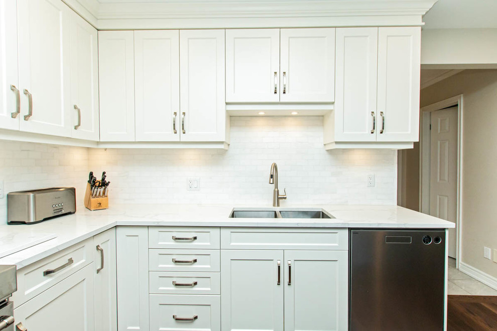 Example of a mid-sized transitional l-shaped medium tone wood floor and brown floor open concept kitchen design with an undermount sink, shaker cabinets, white cabinets, quartzite countertops, white backsplash, stone tile backsplash, stainless steel appliances, an island and white countertops
