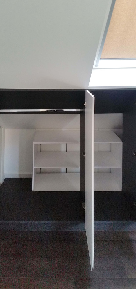 This is an example of a mid-sized modern single-wall utility room in London with white cabinets, white walls, laminate floors and black floor.