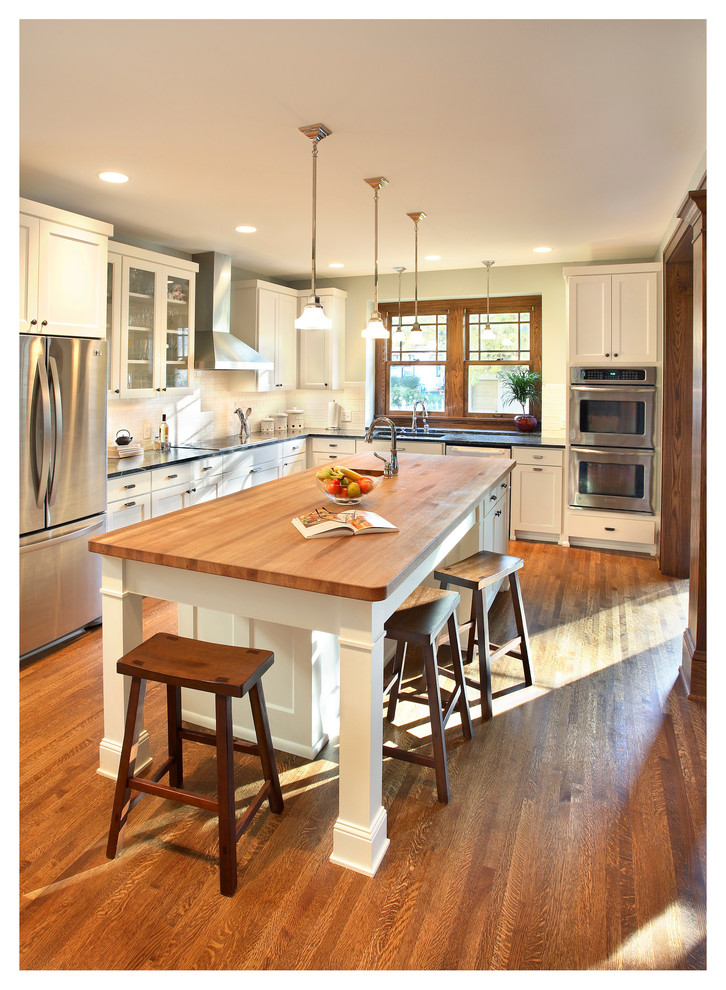 This is an example of a large arts and crafts l-shaped eat-in kitchen in Minneapolis with an undermount sink, shaker cabinets, white cabinets, granite benchtops, white splashback, subway tile splashback, stainless steel appliances, dark hardwood floors and with island.