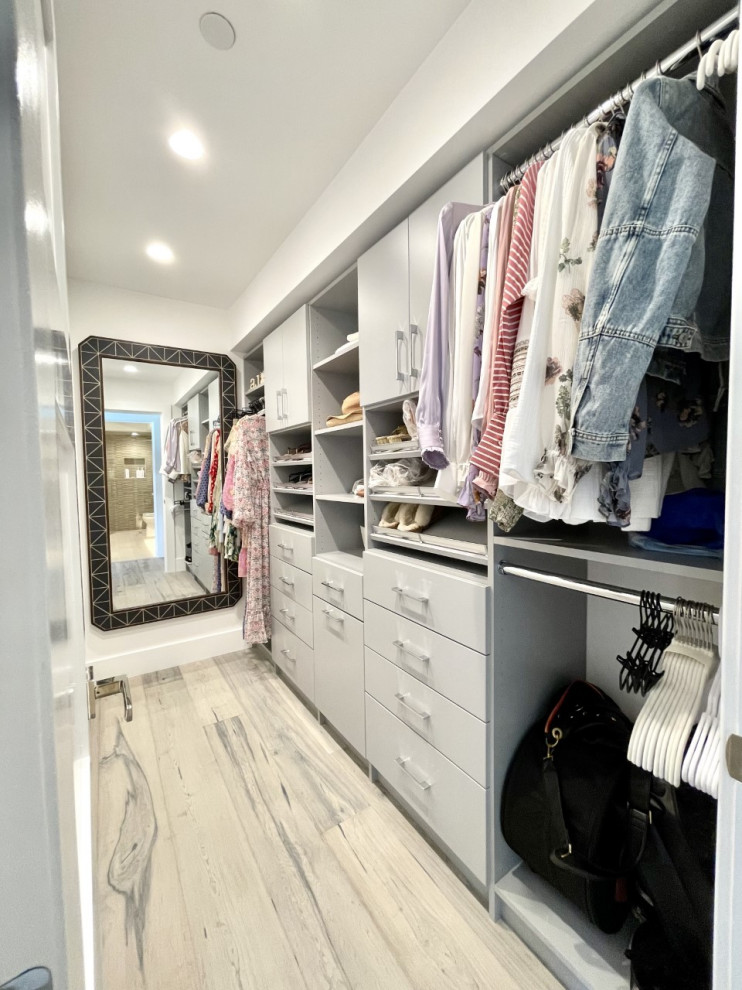 Ejemplo de armario y vestidor de mujer minimalista pequeño con a medida, armarios con paneles lisos, puertas de armario grises, suelo de madera en tonos medios y suelo gris