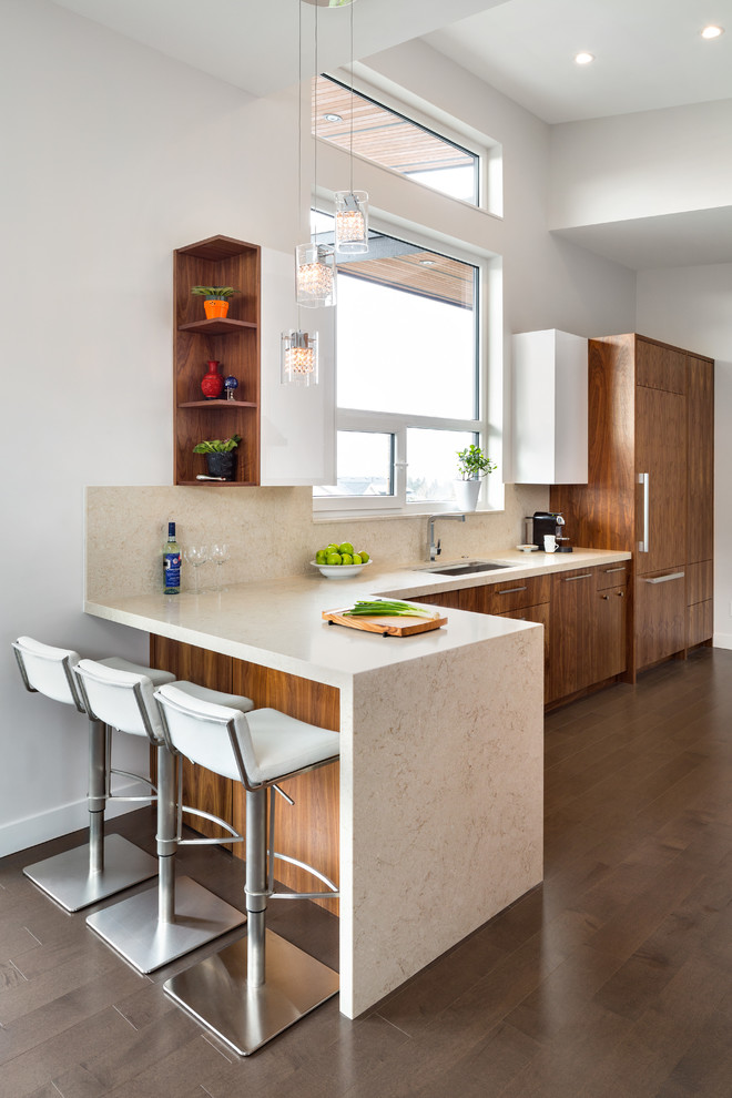 Design ideas for a large contemporary galley eat-in kitchen in Vancouver with a double-bowl sink, flat-panel cabinets, medium wood cabinets, quartz benchtops, beige splashback, stone slab splashback, panelled appliances, dark hardwood floors, a peninsula and beige benchtop.