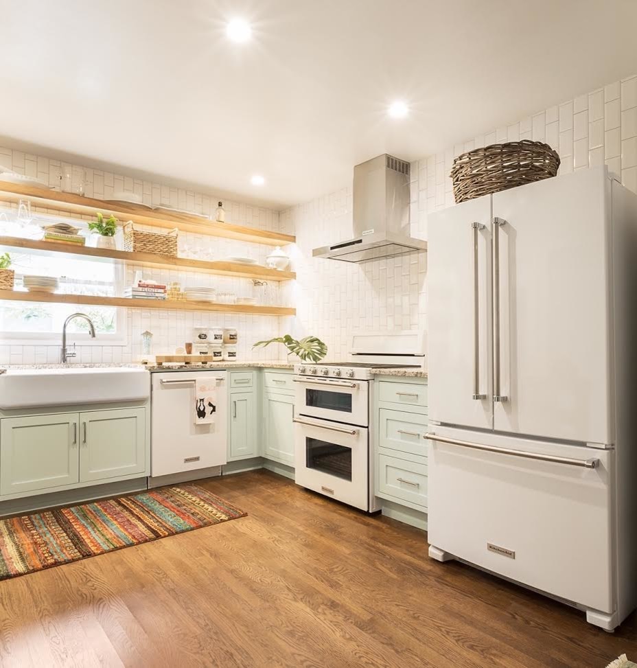 Photo of a mid-sized country l-shaped open plan kitchen in Austin with a farmhouse sink, shaker cabinets, no island, blue cabinets, granite benchtops, white splashback, white appliances, medium hardwood floors and brown floor.