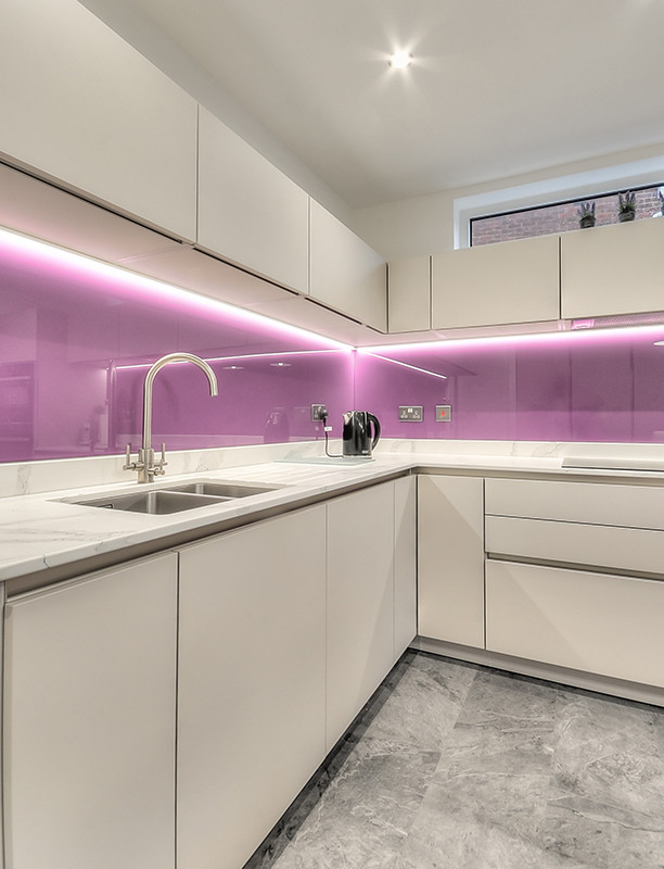 Inspiration for a modern kitchen in Other with a single-bowl sink, flat-panel cabinets, white cabinets, quartzite benchtops, glass sheet splashback, black appliances, vinyl floors, with island, grey floor and pink splashback.