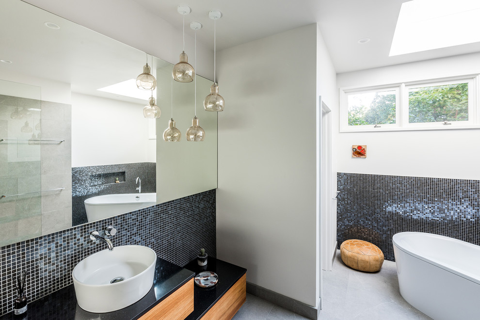 Photo of a contemporary bathroom in Melbourne with medium wood cabinets, a freestanding tub, an open shower, a one-piece toilet, gray tile, porcelain tile, white walls, porcelain floors, a vessel sink and engineered quartz benchtops.