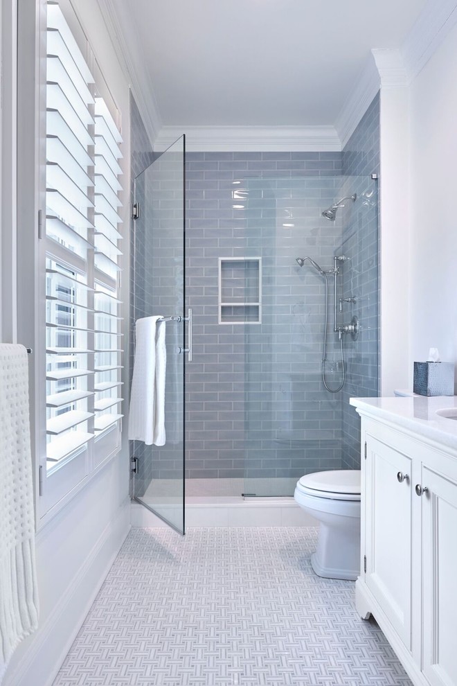Photo of a mid-sized traditional 3/4 bathroom in New York with recessed-panel cabinets, white cabinets, an alcove shower, a two-piece toilet, blue tile, ceramic tile, white walls, marble floors, an undermount sink, marble benchtops, white floor and a hinged shower door.