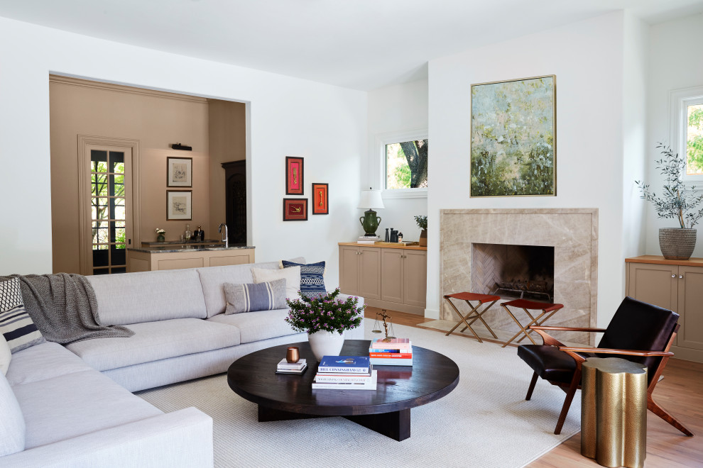 Modelo de sala de estar abierta clásica renovada grande con paredes blancas, suelo de madera en tonos medios, todas las chimeneas, marco de chimenea de piedra y suelo blanco