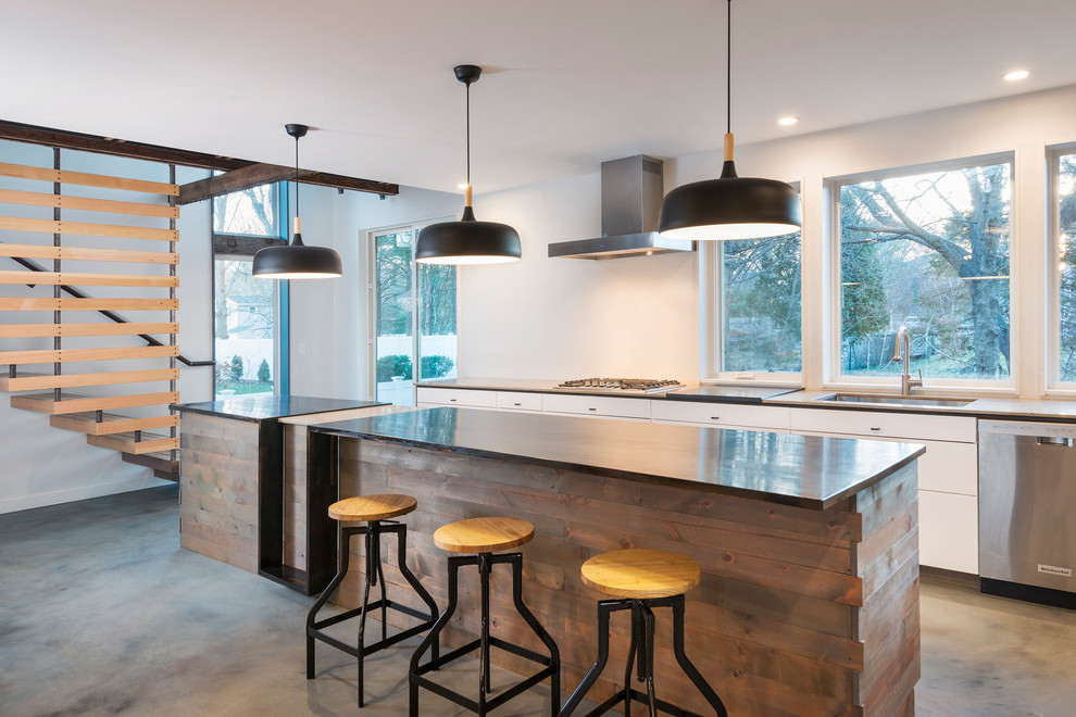 This is an example of an industrial kitchen in Providence with an undermount sink, flat-panel cabinets, white cabinets, window splashback, concrete floors, with island, grey floor and black benchtop.
