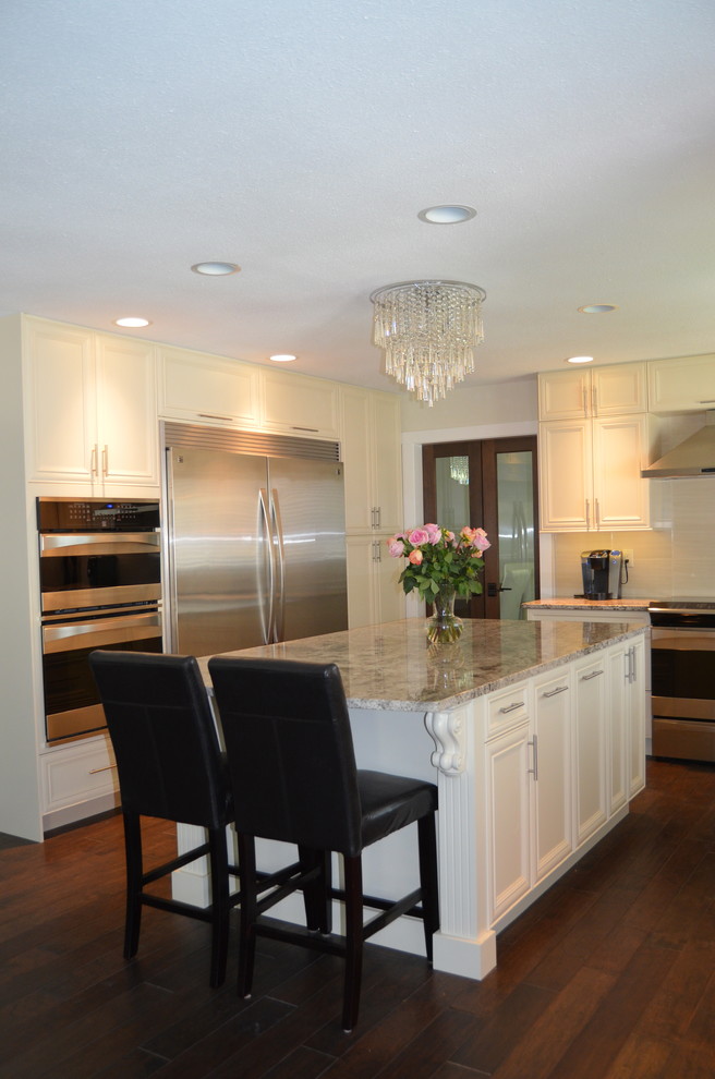 This is an example of a traditional u-shaped eat-in kitchen in Vancouver with a farmhouse sink, flat-panel cabinets, white cabinets, granite benchtops and stainless steel appliances.