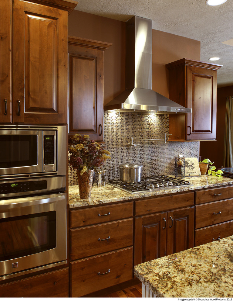 Mountain style l-shaped dark wood floor and brown floor eat-in kitchen photo with a farmhouse sink, raised-panel cabinets, medium tone wood cabinets, granite countertops, multicolored backsplash, mosaic tile backsplash, stainless steel appliances and an island