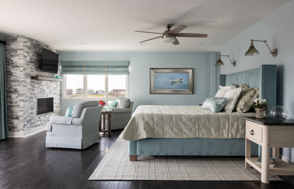 ニューヨークにある巨大なビーチスタイルのおしゃれな主寝室 (青い壁、濃色無垢フローリング、標準型暖炉、積石の暖炉まわり、茶色い床、アクセントウォール、白い天井) のインテリア