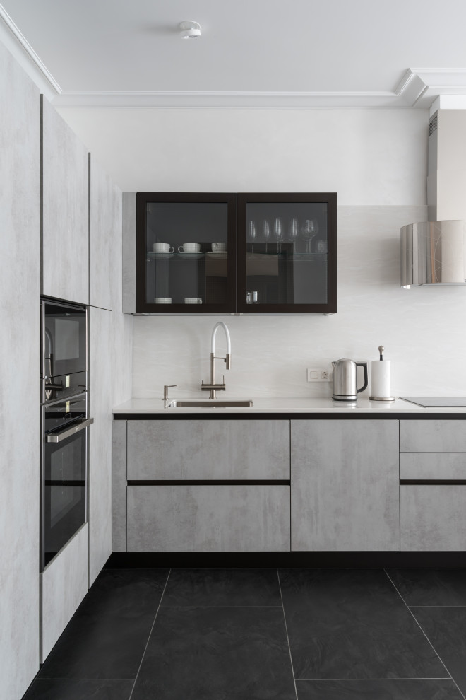Photo of a mid-sized contemporary l-shaped kitchen in Saint Petersburg with an undermount sink, flat-panel cabinets, grey cabinets, solid surface benchtops, white splashback, porcelain floors, black floor, white benchtop and panelled appliances.