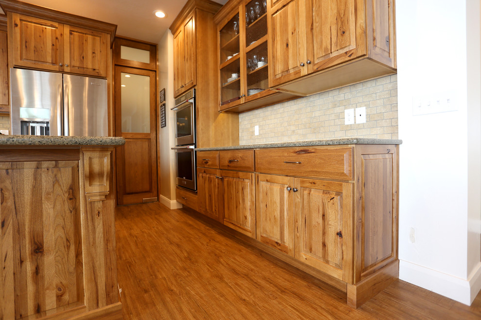 Photo of a large country u-shaped eat-in kitchen in Salt Lake City with an undermount sink, raised-panel cabinets, medium wood cabinets, granite benchtops, beige splashback, ceramic splashback, stainless steel appliances, vinyl floors and with island.