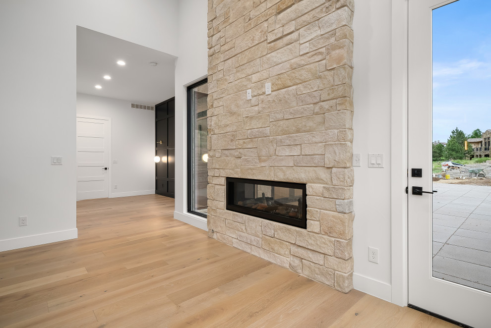 This is an example of a large midcentury master bedroom in Denver with black walls, light hardwood floors, a two-sided fireplace, a stone fireplace surround and brown floor.