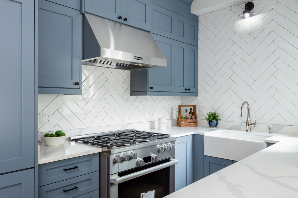 Inredning av ett klassiskt mycket stort vit vitt kök, med en integrerad diskho, luckor med lamellpanel, blå skåp, bänkskiva i kvarts, vitt stänkskydd, stänkskydd i stenkakel, rostfria vitvaror, ljust trägolv, en köksö och beiget golv