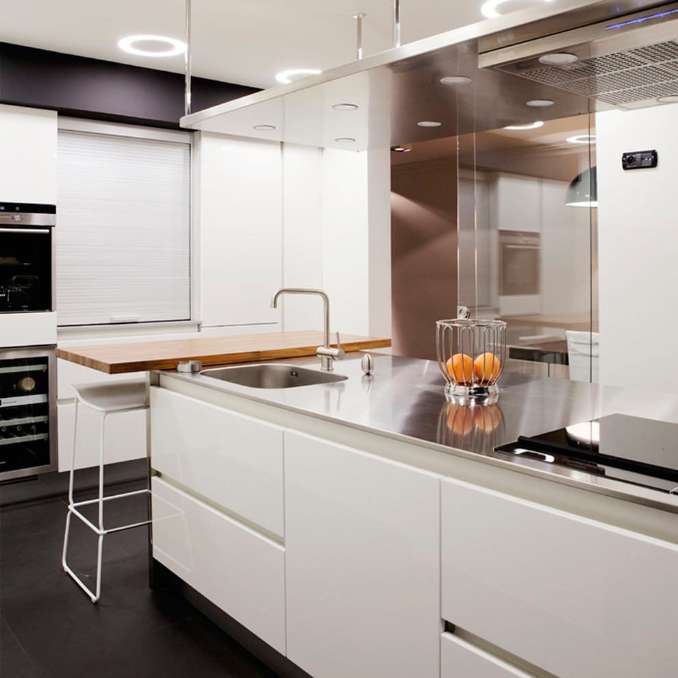 Photo of a modern kitchen in Other with an integrated sink, flat-panel cabinets, white cabinets, stainless steel benchtops, panelled appliances, porcelain floors and with island.