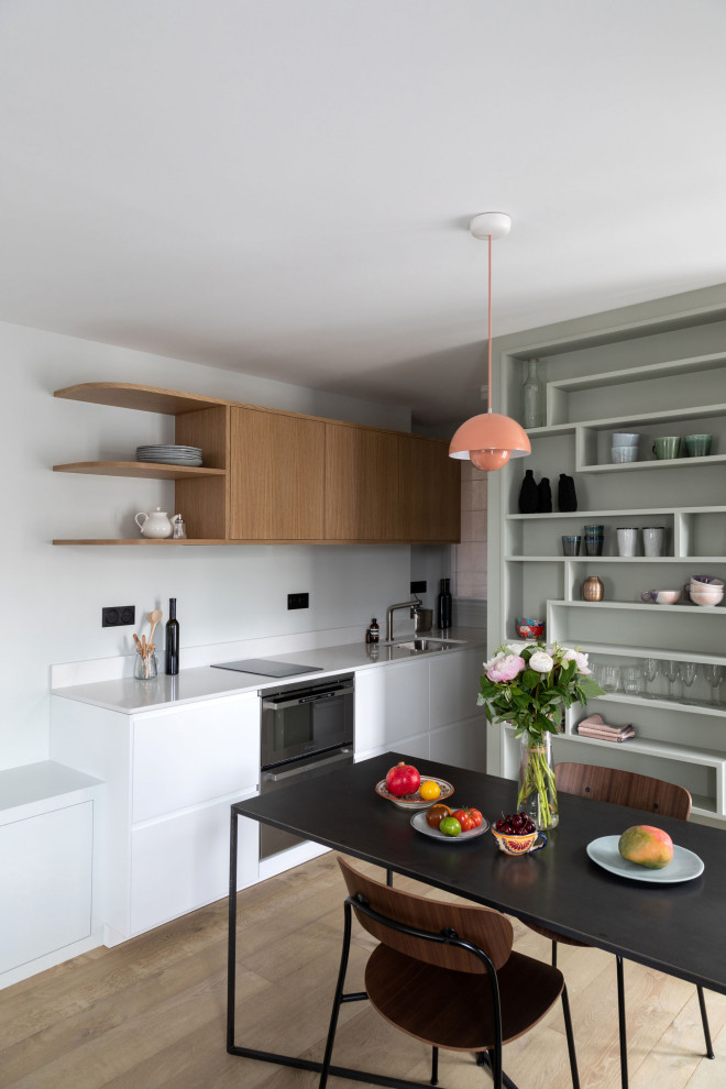 Small modern single-wall open plan kitchen in Paris with an integrated sink, flat-panel cabinets, white cabinets, marble benchtops, white splashback, marble splashback, stainless steel appliances, light hardwood floors, no island, beige floor and white benchtop.