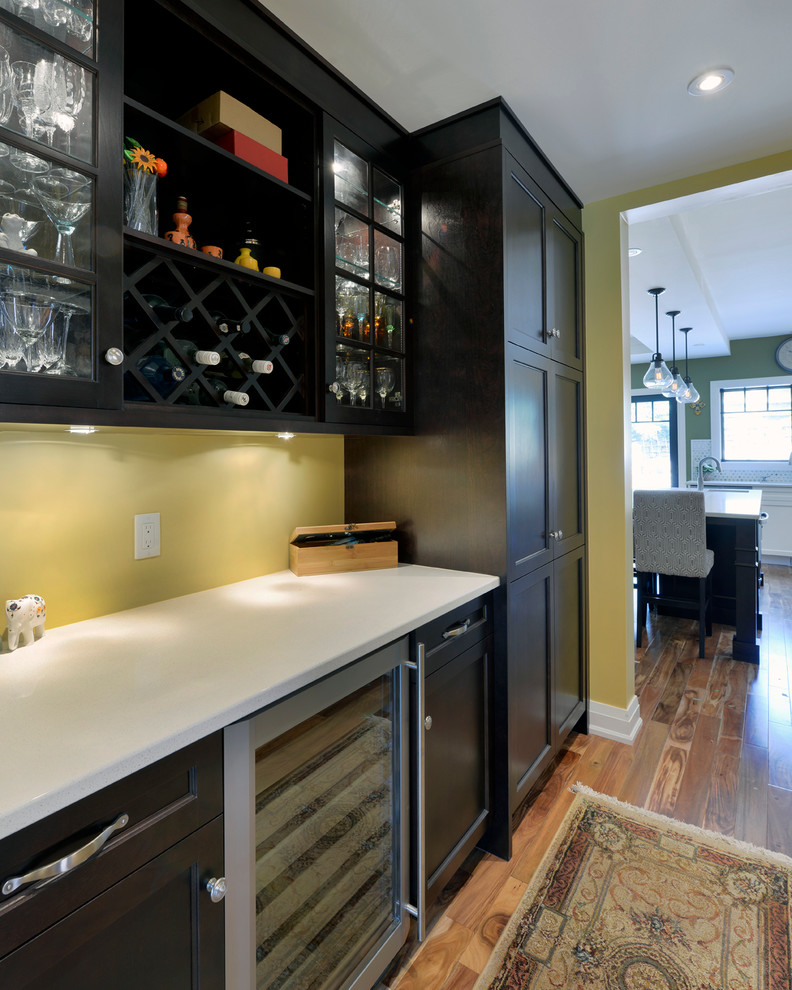 Photo of a mid-sized arts and crafts single-wall kitchen pantry in Ottawa with shaker cabinets, dark wood cabinets, quartz benchtops, stainless steel appliances, medium hardwood floors and yellow splashback.