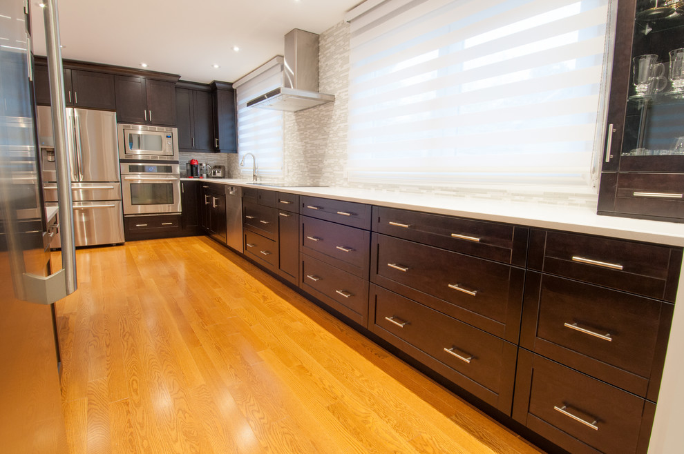 Large transitional galley light wood floor enclosed kitchen photo in Toronto with a single-bowl sink, shaker cabinets, dark wood cabinets, quartzite countertops, beige backsplash, stone tile backsplash, stainless steel appliances and an island