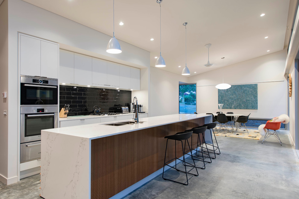 Photo of a contemporary galley eat-in kitchen in Canberra - Queanbeyan with a double-bowl sink, flat-panel cabinets, white cabinets, black splashback, stainless steel appliances, concrete floors and with island.