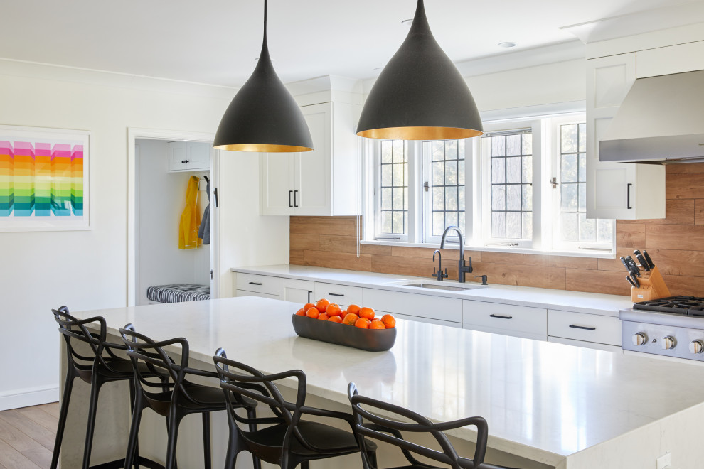 Example of a large transitional u-shaped light wood floor and brown floor enclosed kitchen design in New York with an undermount sink, shaker cabinets, white cabinets, quartz countertops, brown backsplash, wood backsplash, stainless steel appliances, an island and white countertops