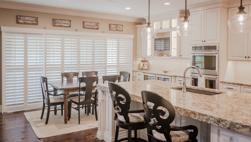 Large transitional l-shaped kitchen photo in St Louis with an undermount sink, raised-panel cabinets, white cabinets, granite countertops, beige backsplash, subway tile backsplash, stainless steel appliances and an island