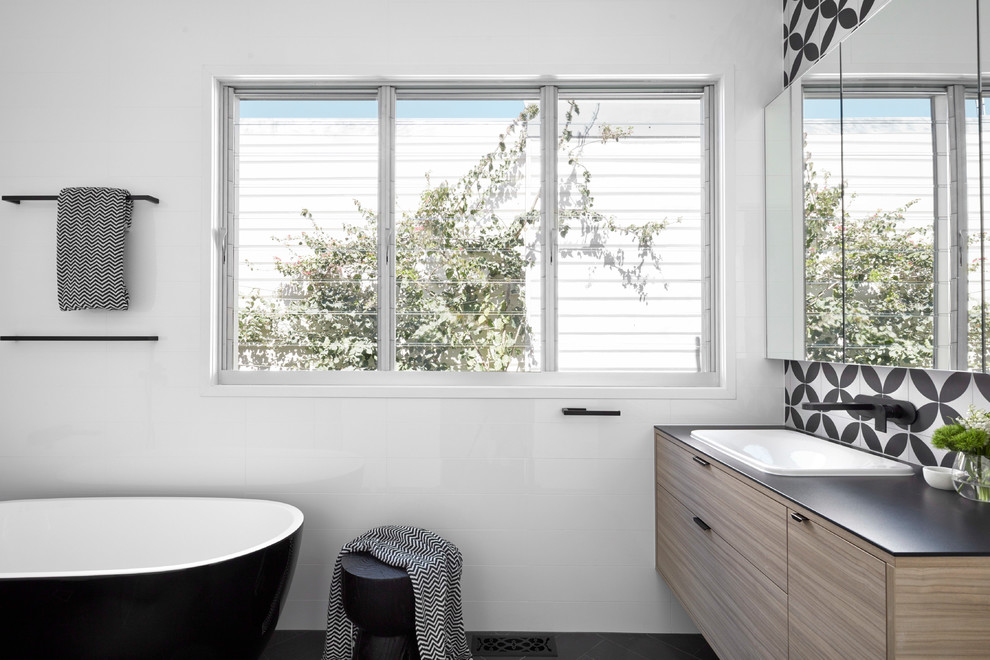 Photo of a mid-sized contemporary master bathroom in Melbourne with beaded inset cabinets, light wood cabinets, a freestanding tub, an open shower, multi-coloured tile, mosaic tile, a drop-in sink, solid surface benchtops and black benchtops.