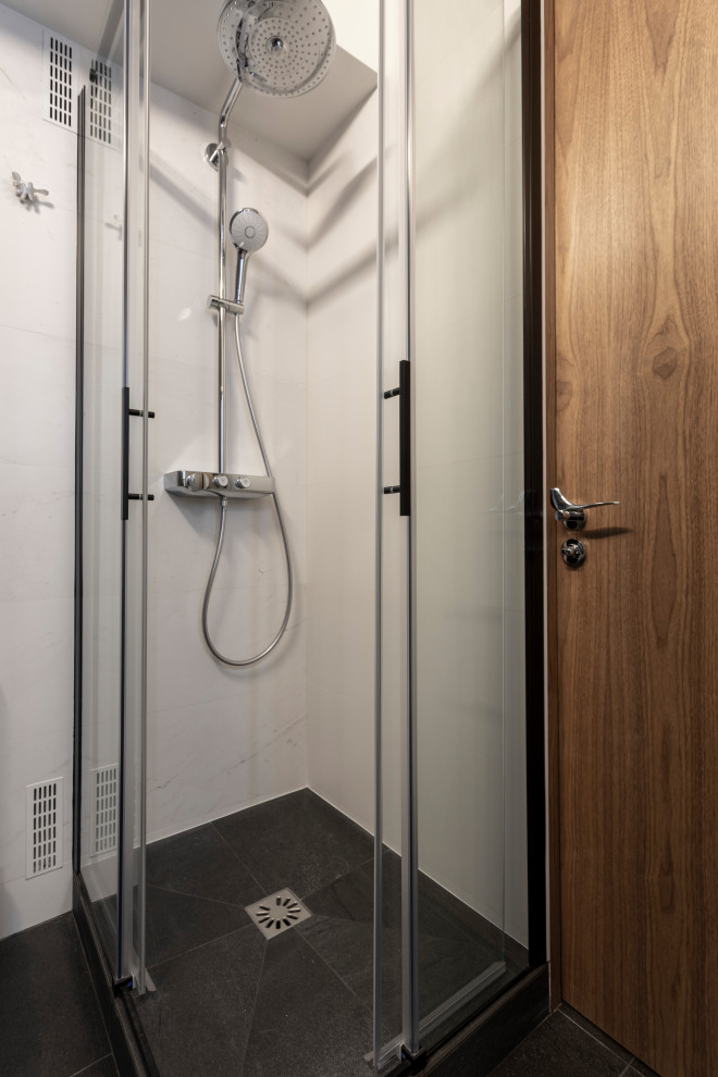 This is an example of a small contemporary grey and black shower room bathroom in Paris with beaded cabinets, black cabinets, a corner shower, a one-piece toilet, white tiles, ceramic tiles, white walls, ceramic flooring, a console sink, solid surface worktops, black floors, a sliding door, white worktops, a laundry area, a single sink and a built in vanity unit.