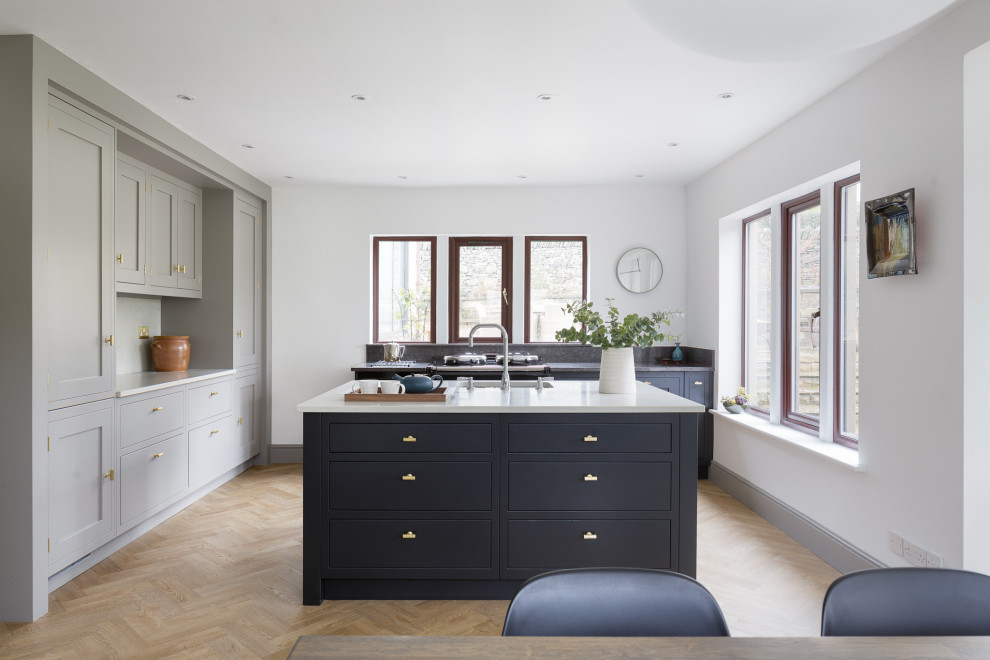 Transitional u-shaped eat-in kitchen in Other with an undermount sink, shaker cabinets, grey cabinets, white splashback, panelled appliances, medium hardwood floors, with island, brown floor and white benchtop.
