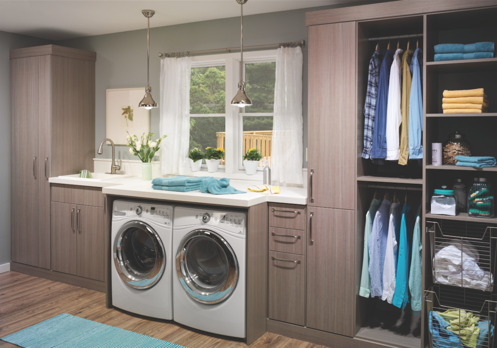 This is an example of a mid-sized transitional single-wall dedicated laundry room in Columbus with an undermount sink, flat-panel cabinets, medium wood cabinets, solid surface benchtops, grey walls, medium hardwood floors and a side-by-side washer and dryer.