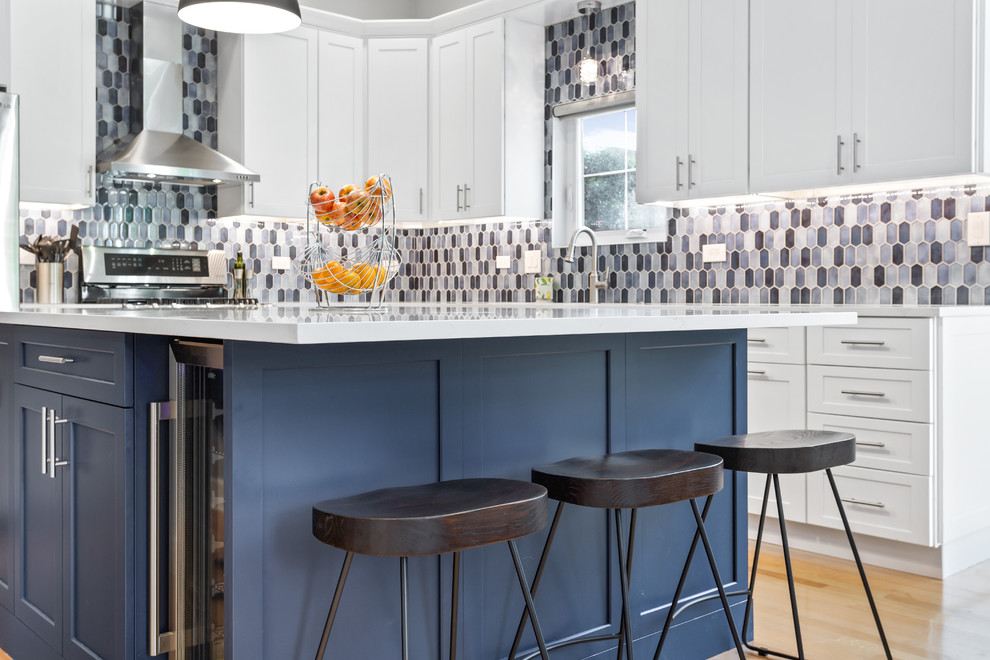 Mid-sized contemporary l-shaped eat-in kitchen in Chicago with an undermount sink, shaker cabinets, white cabinets, quartz benchtops, multi-coloured splashback, mosaic tile splashback, stainless steel appliances, medium hardwood floors, with island and white benchtop.