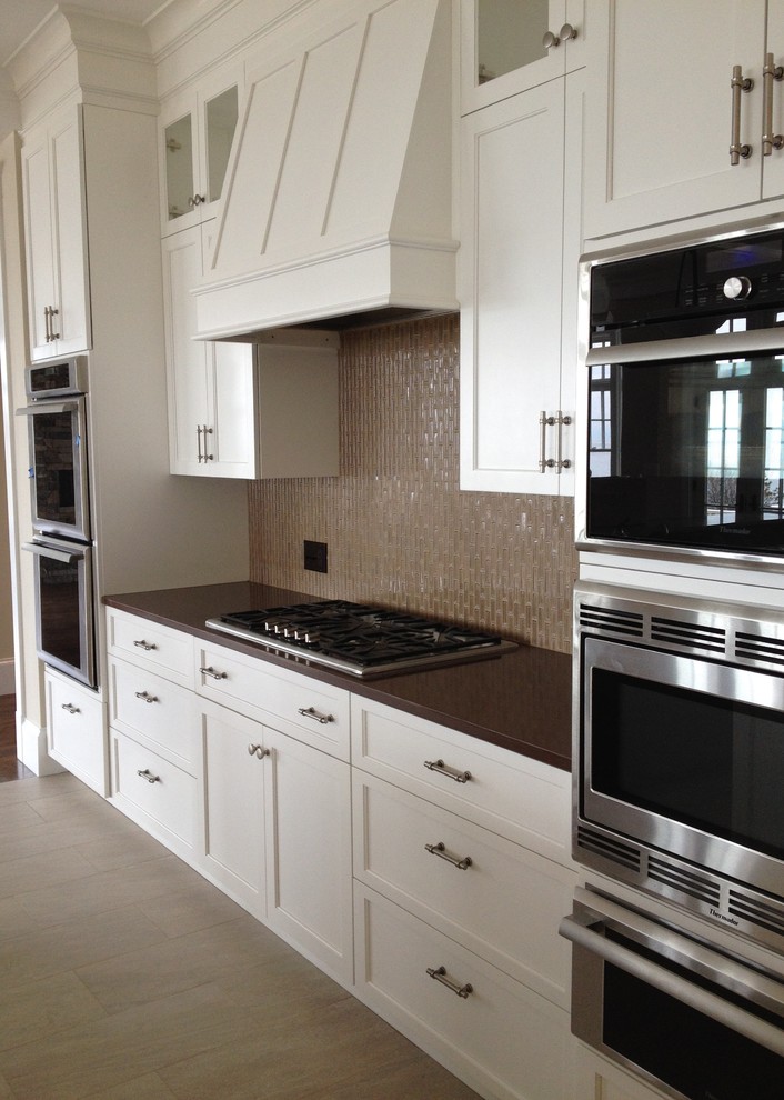 Inspiration for a transitional ceramic tile eat-in kitchen remodel in Boston with a double-bowl sink, recessed-panel cabinets, white cabinets, quartz countertops, brown backsplash, glass tile backsplash, stainless steel appliances and an island
