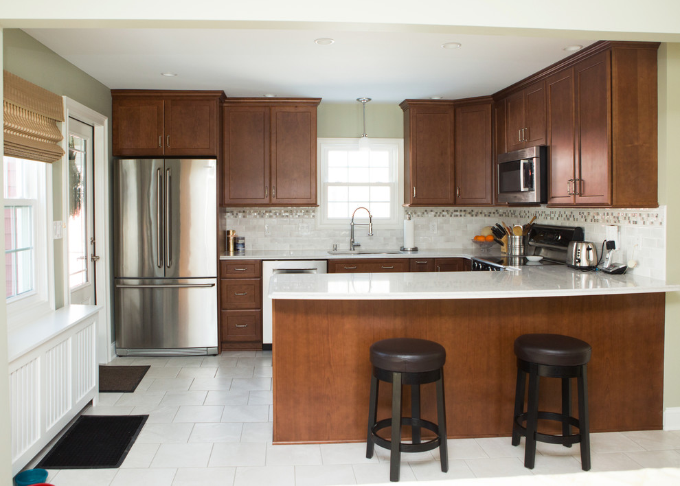 Mid-sized transitional l-shaped white floor and ceramic tile eat-in kitchen photo with an undermount sink, quartz countertops, white backsplash, stainless steel appliances, white countertops, shaker cabinets, medium tone wood cabinets, porcelain backsplash and a peninsula
