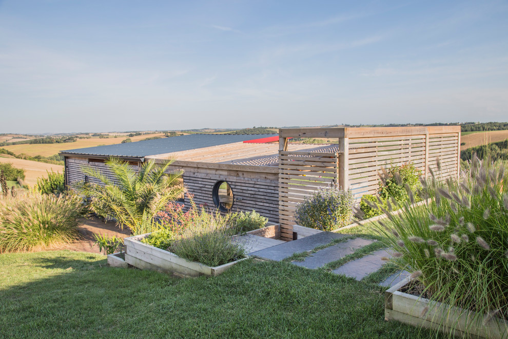 Aménagement d'un grand jardin arrière contemporain l'été avec un mur de soutènement, une exposition ensoleillée et une terrasse en bois.