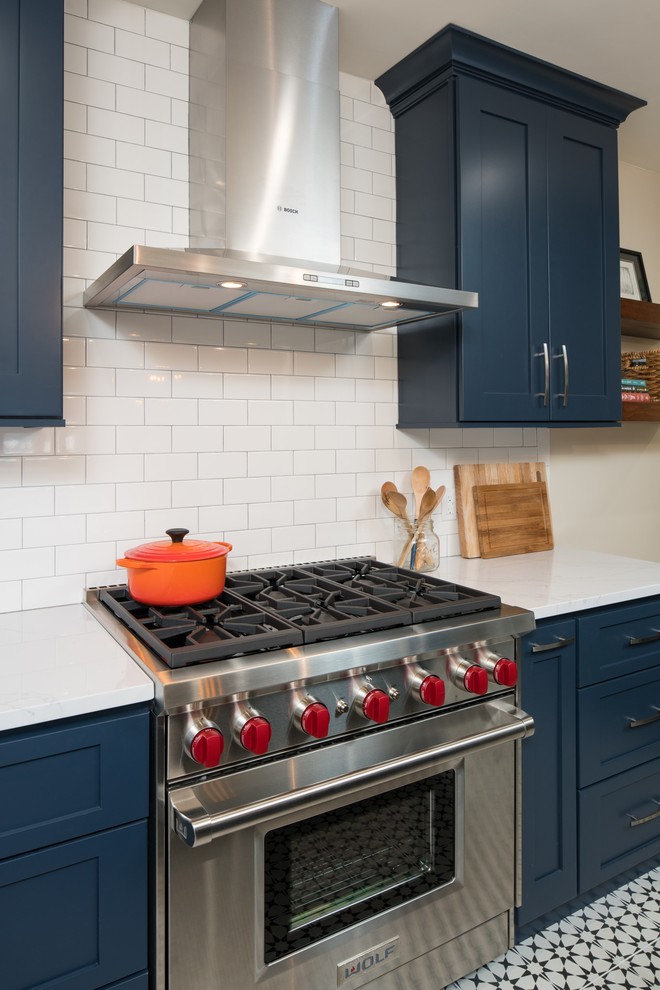 Design ideas for a small eclectic l-shaped eat-in kitchen in Seattle with a farmhouse sink, raised-panel cabinets, blue cabinets, quartzite benchtops, white splashback, ceramic splashback, stainless steel appliances, cement tiles, with island and black floor.