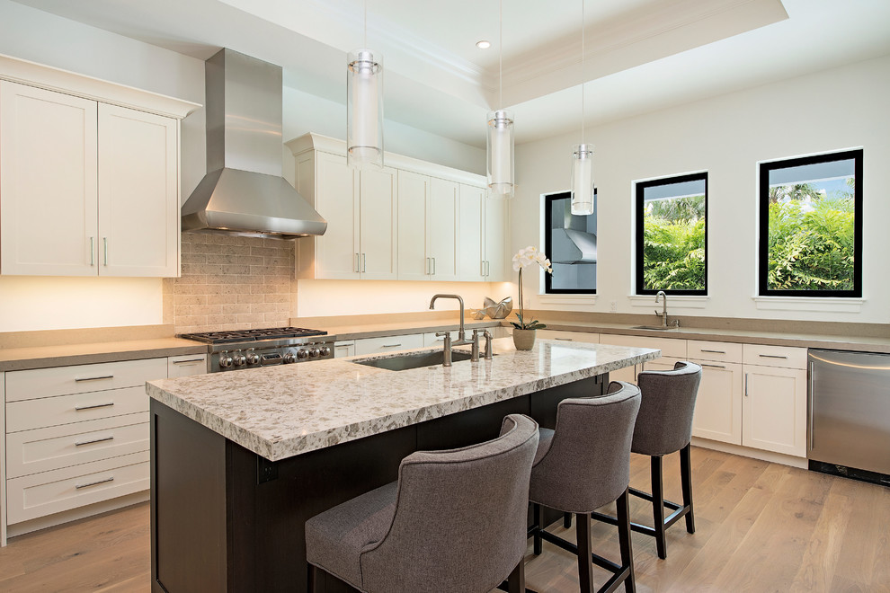 Eat-in kitchen - large transitional l-shaped medium tone wood floor eat-in kitchen idea in Miami with a drop-in sink, recessed-panel cabinets, white cabinets, beige backsplash, brick backsplash, stainless steel appliances and an island