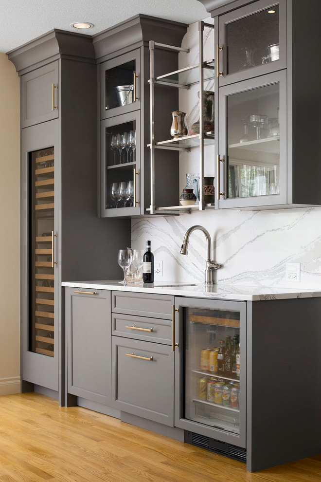 Photo of a transitional single-wall wet bar in Calgary with an undermount sink, glass-front cabinets, grey cabinets, white splashback, light hardwood floors, beige floor, marble benchtops, marble splashback and white benchtop.