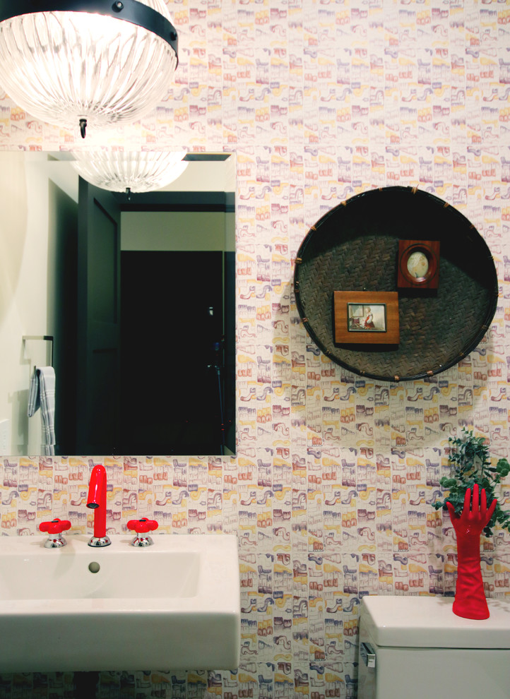 This is an example of a small country powder room in San Diego with a wall-mount toilet, beige tile, beige walls, light hardwood floors, a wall-mount sink and grey floor.