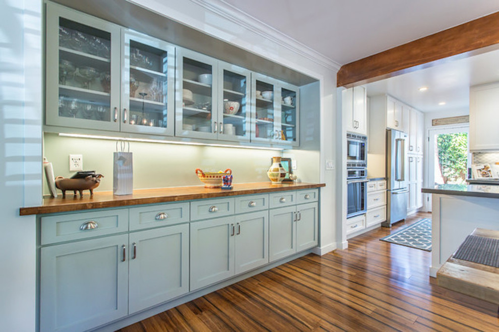 Example of a mid-sized transitional u-shaped bamboo floor and brown floor eat-in kitchen design in Orange County with recessed-panel cabinets, blue cabinets, wood countertops, blue backsplash, stainless steel appliances, an island and brown countertops