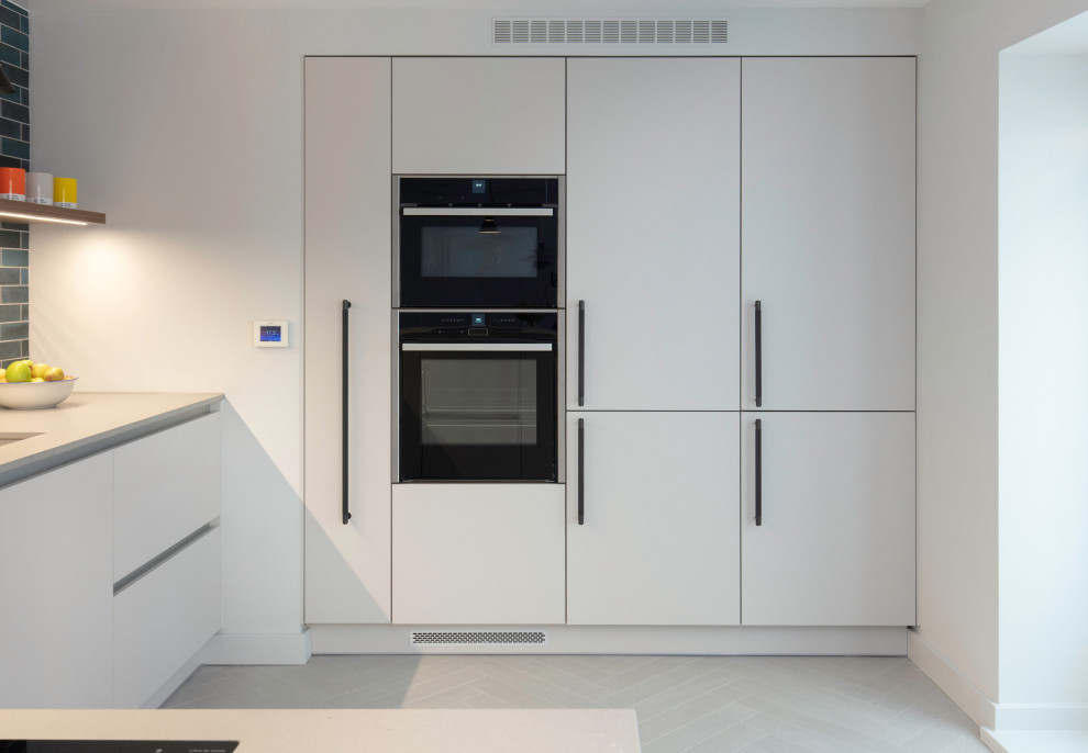 Example of a mid-sized minimalist l-shaped light wood floor and beige floor eat-in kitchen design in London with a drop-in sink, flat-panel cabinets, white cabinets, quartzite countertops, blue backsplash, subway tile backsplash, stainless steel appliances, a peninsula and white countertops