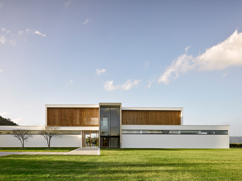 This is an example of an expansive contemporary two-storey concrete white house exterior in Brisbane with a flat roof and a metal roof.